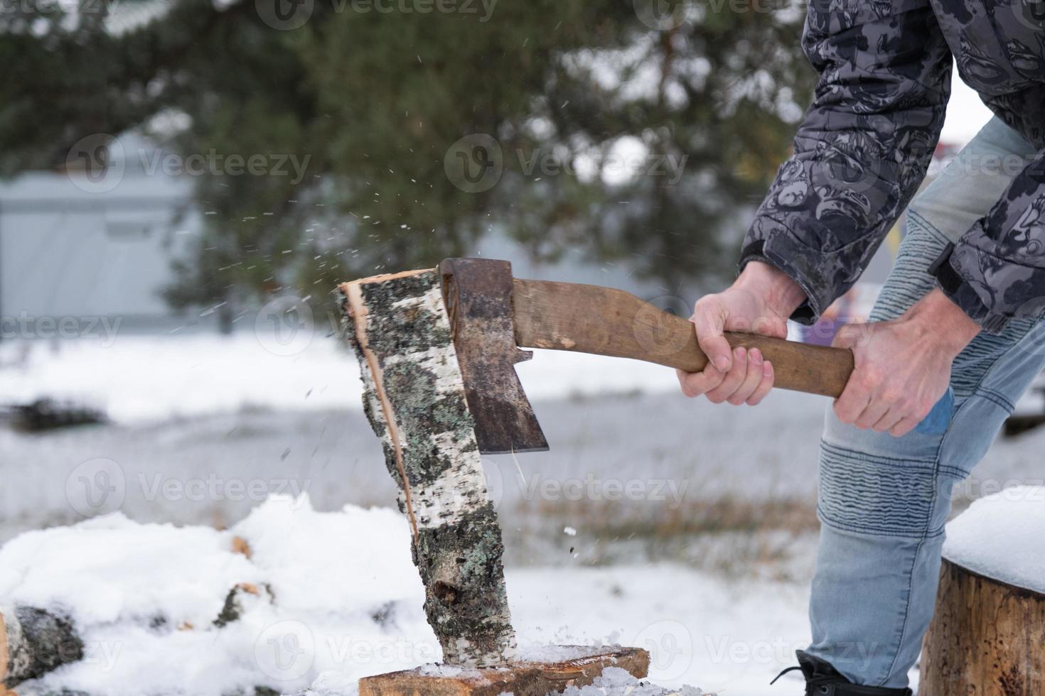 un' uomo è chopping legna da ardere con un ascia nel inverno all'aperto nel il neve. alternativa il riscaldamento, legna raccolta, energia crisi foto