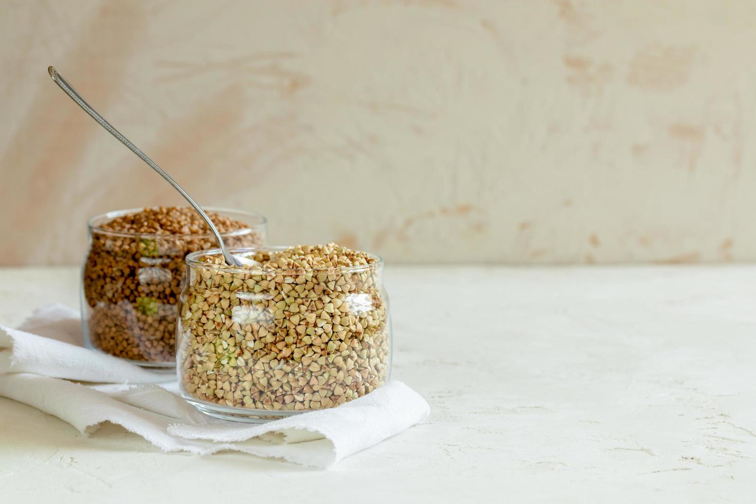 Due lattine di grano saraceno e cucchiaio su bianca tavolo con copia spazio. foto