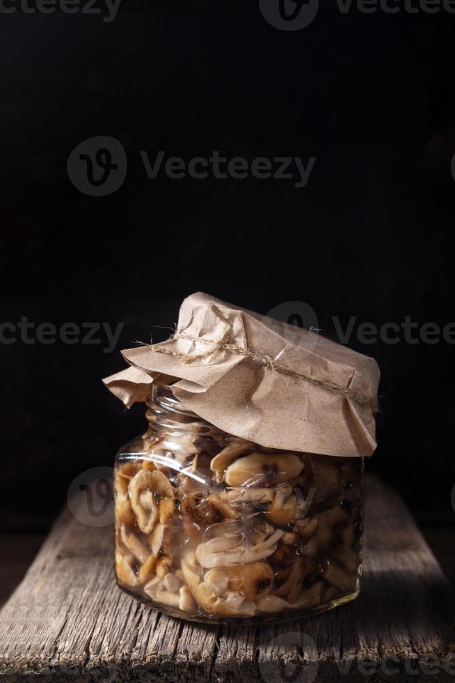 uno bicchiere vaso con sottaceto foresta funghi miele agarici sotto carta copertina su vecchio di legno tavola su nero sfondo. foto