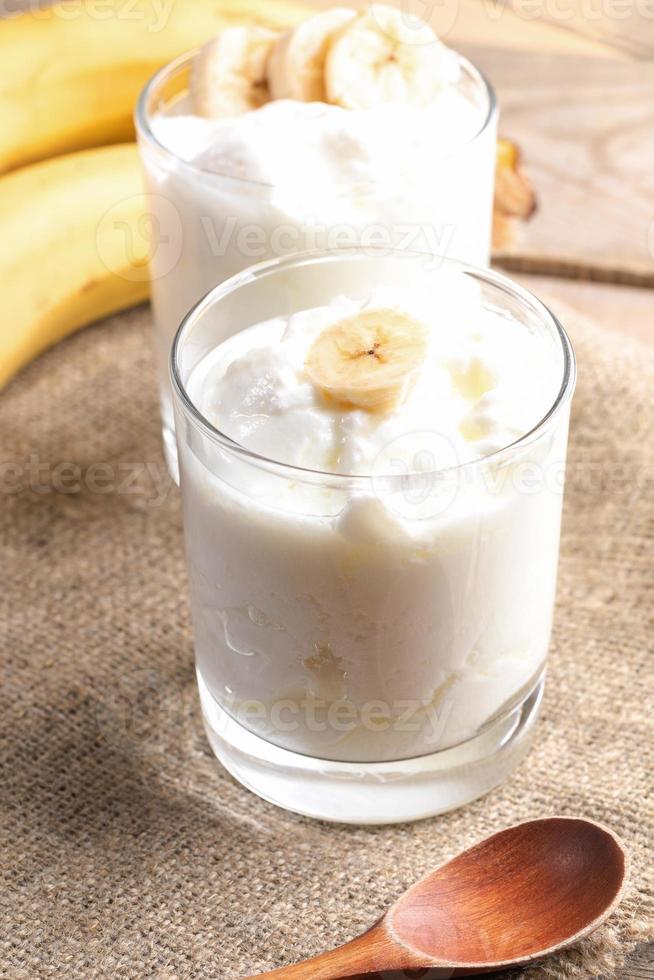 Due bicchieri di Grasso fatti in casa Yogurt con Banana fette su tela ruvida tovagliolo. foto