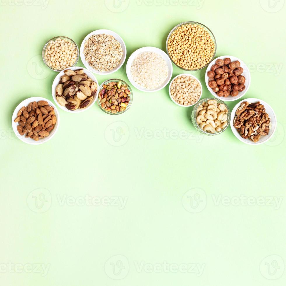 diverso noccioline e cereali nel ciotole su due toni beige-verde sfondo. superiore Visualizza. copia spazio. foto
