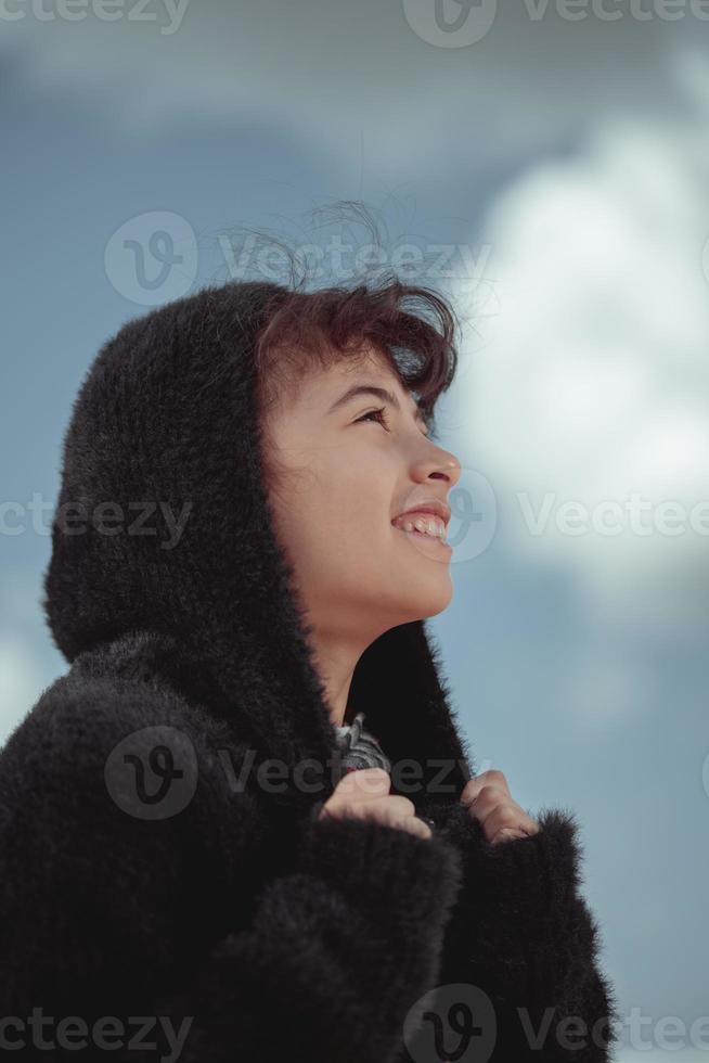 ragazza nel un' nero pelliccia cappotto sorridente sotto un' blu cielo con nuvole foto