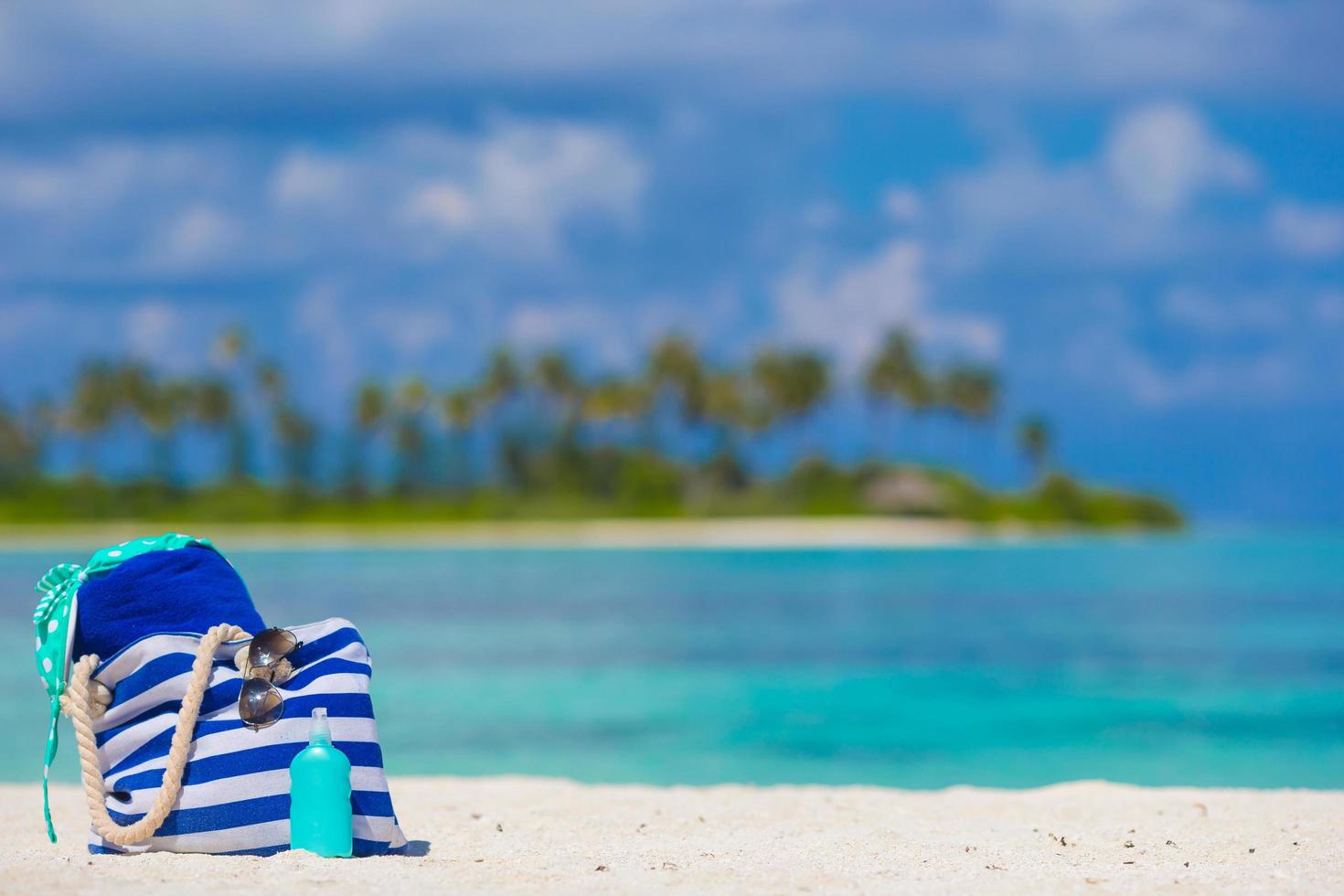 borsa con occhiali da sole e crema solare su una spiaggia foto