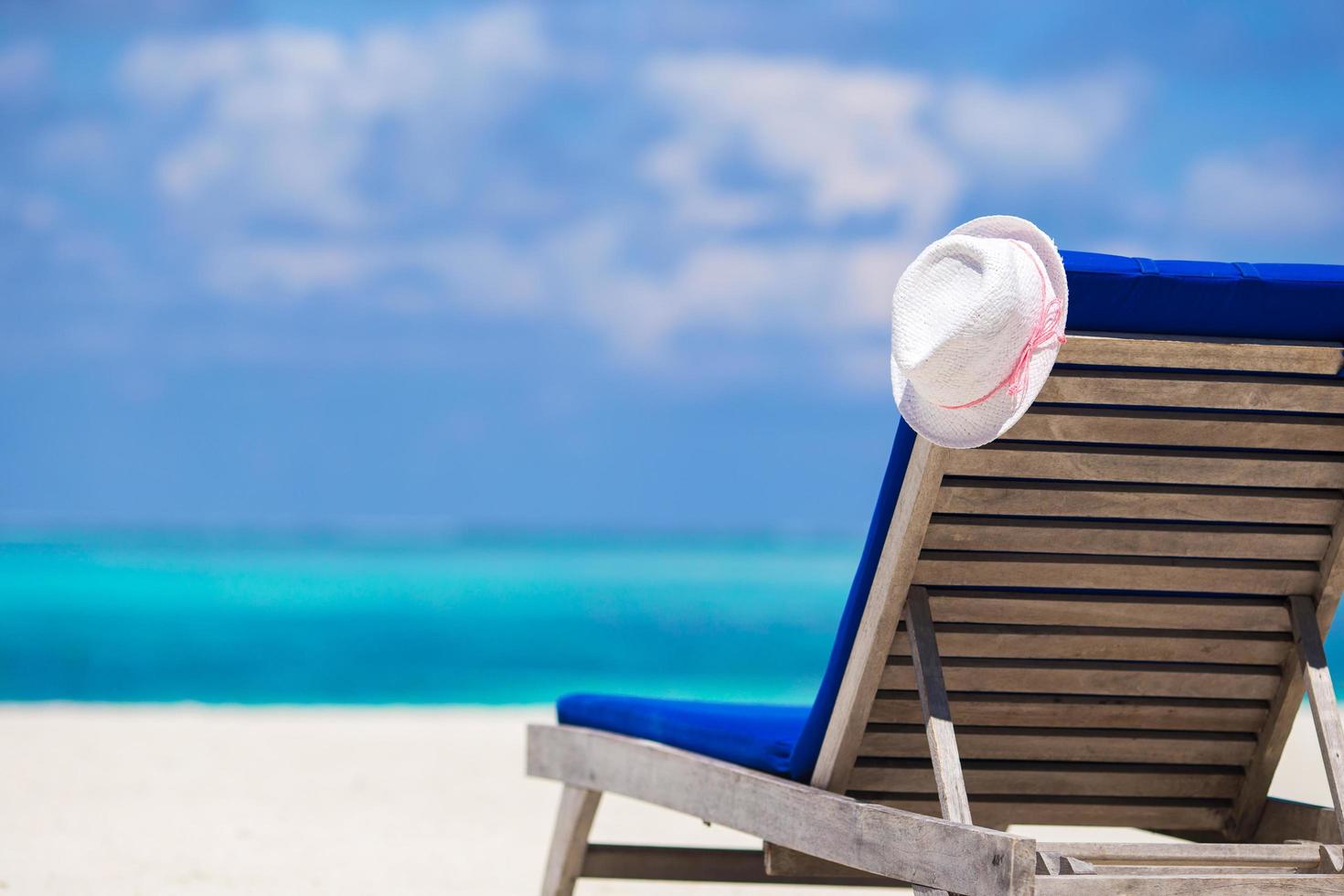 primo piano di una sedia a sdraio e cappello bianco su una spiaggia foto