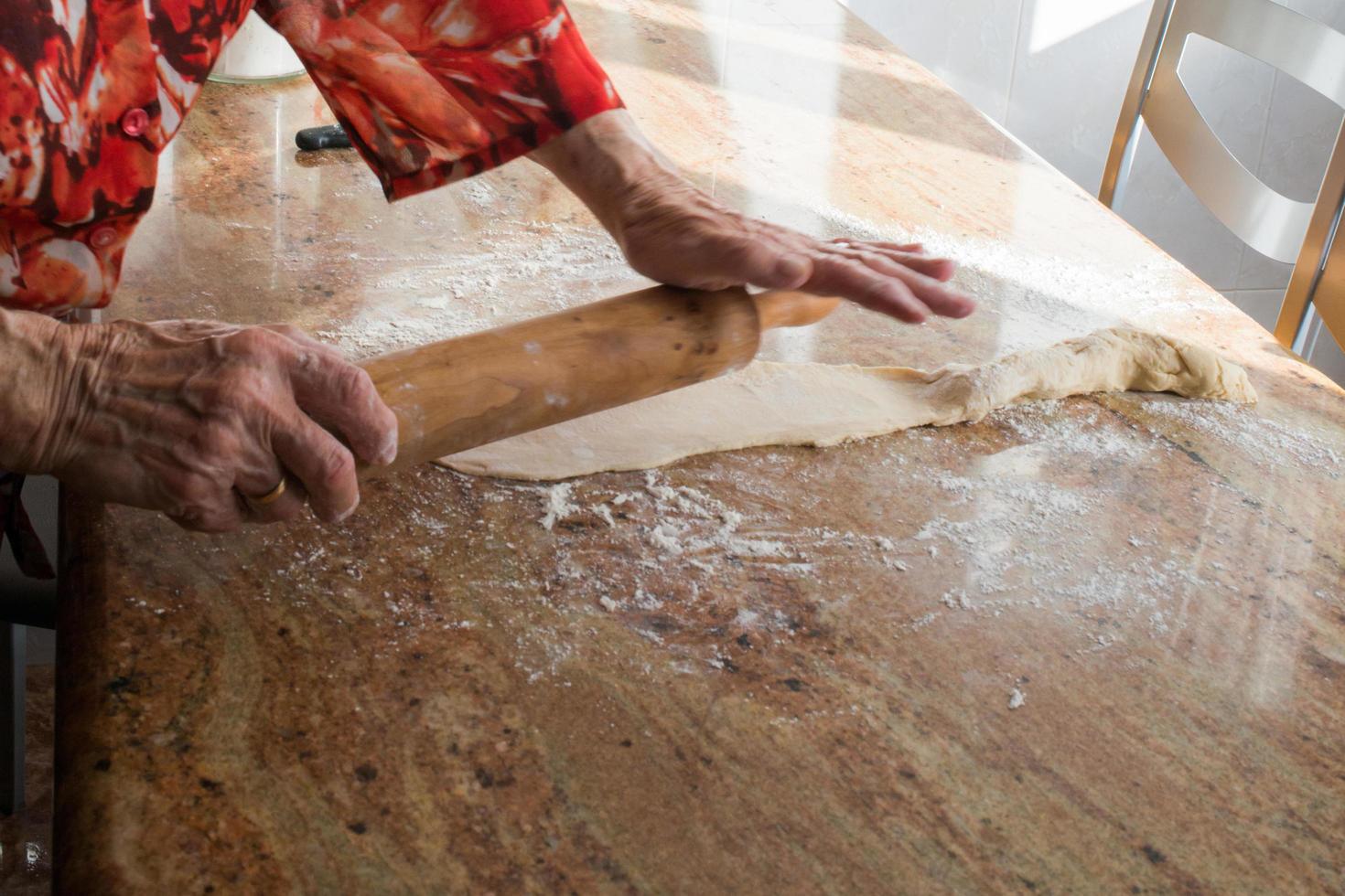 tipico asturiano Natale dolce. anziano donna mani con un' rotolamento perno preparazione con casadielles Impasto. tradicional gastronomia foto