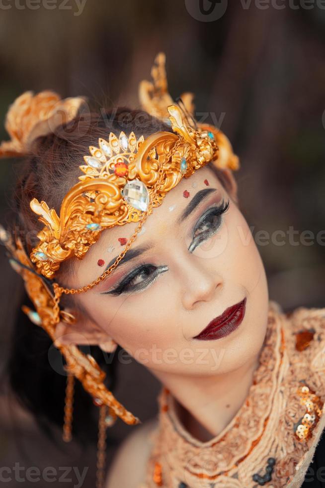 avvicinamento viso di un asiatico donna nel trucco indossare oro corona e oro Accessori con bellissimo facce foto