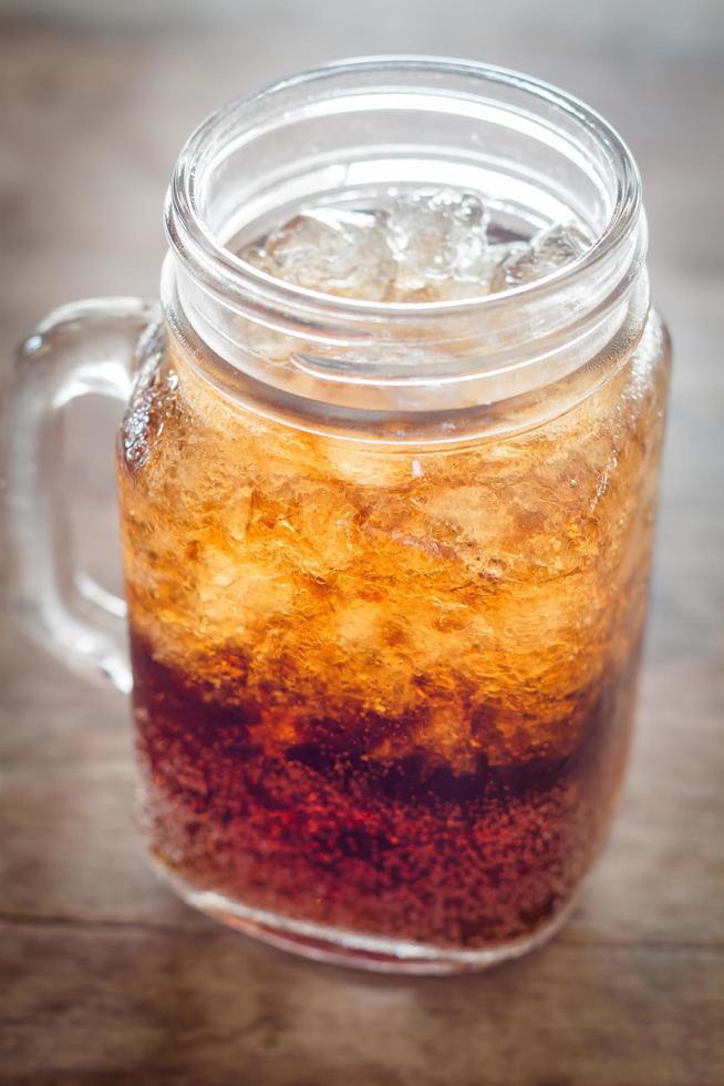 bicchiere di cola con ghiaccio su un tavolo di legno foto