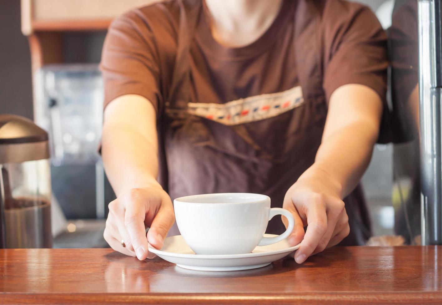 barista che offre una tazza di caffè bianca foto