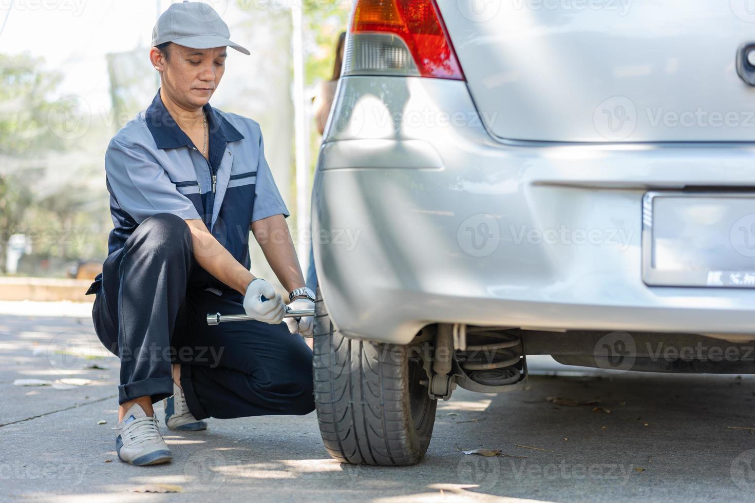 esperto meccanico uomo in uniforme che usa la forza cercando di svitare i dadi dei bulloni delle ruote e aiutare una donna a cambiare la ruota dell'auto in autostrada, servizio auto, riparazione, concetto di manutenzione. foto