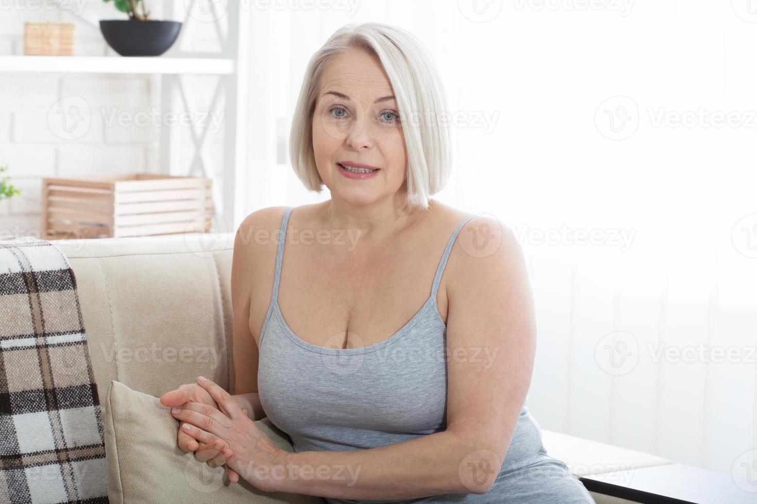 attivo bellissimo di mezza età donna sorridente amichevole e guardare nel telecamera nel vivente camera. donna di viso vicino su. realistico immagini senza ritocco con loro proprio imperfezioni. selettivo messa a fuoco. foto