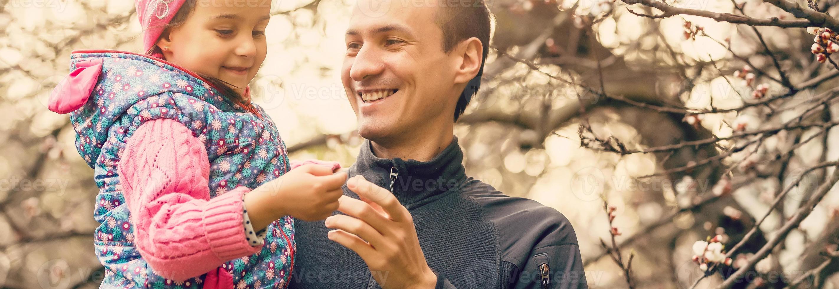 ritratto di un' poco ragazza baci sua papà su guancia. bella ragazza dando un' bacio per sua padre all'aperto. amorevole bambino abbraccio e baci sua padre. foto