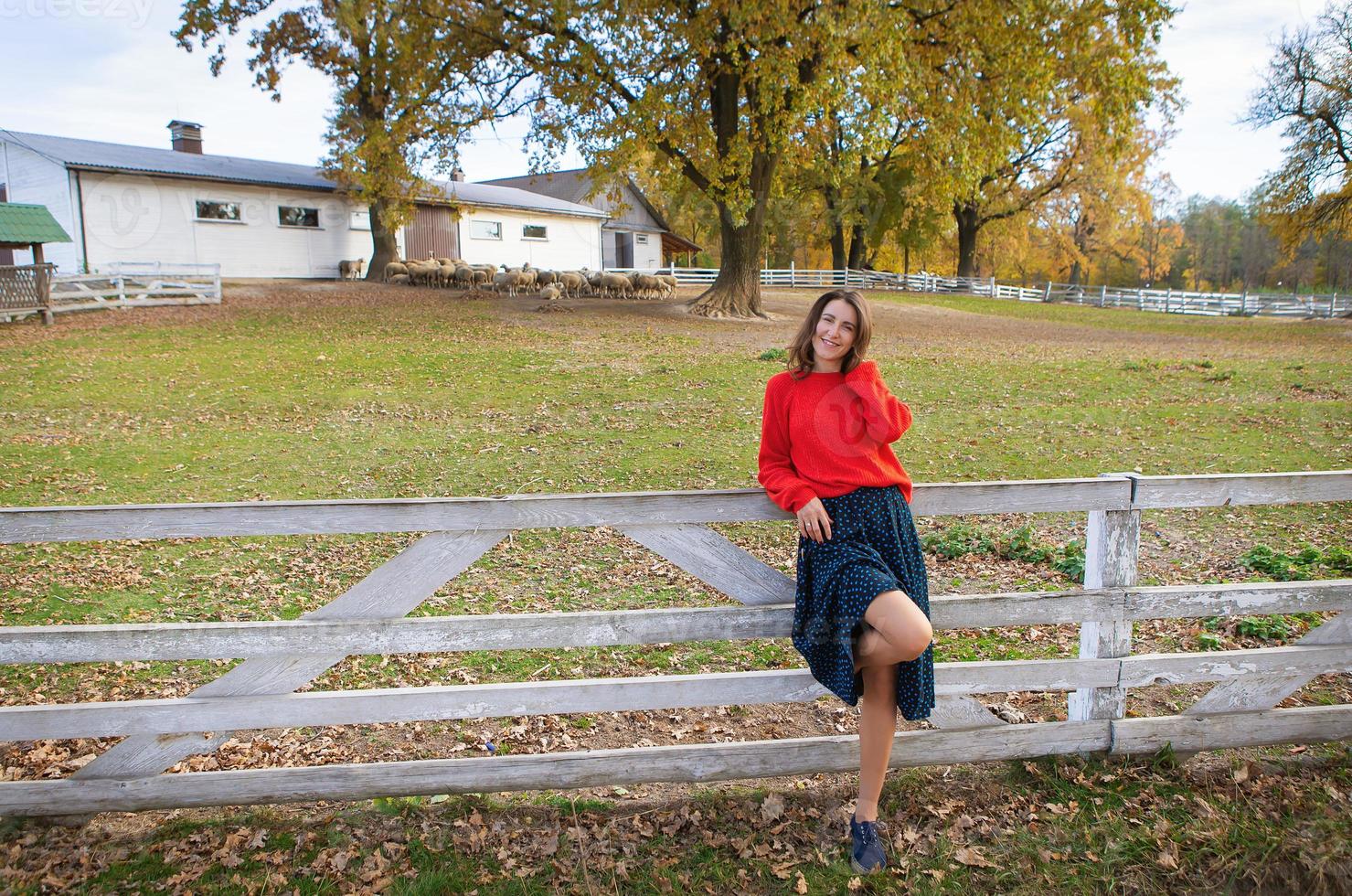 un' bellissimo ragazza nel un' rosso maglione sta vicino un' bianca di legno recinzione. bellissimo caldo autunno. foto