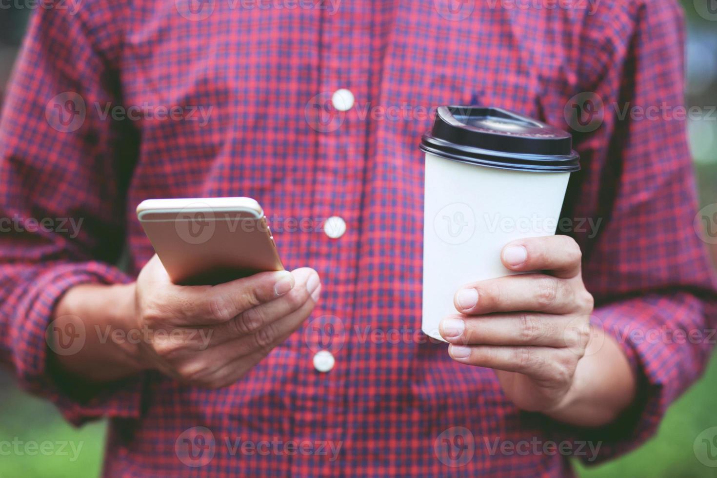 giovane donna signora attraente chat su sua mobile smartphone, tavoletta lettura testo Messaggio su cellula mentre rilassante nel il pubblico parco, hold mano caffè tazza in piedi potabile caffè con nel accogliente mattina foto