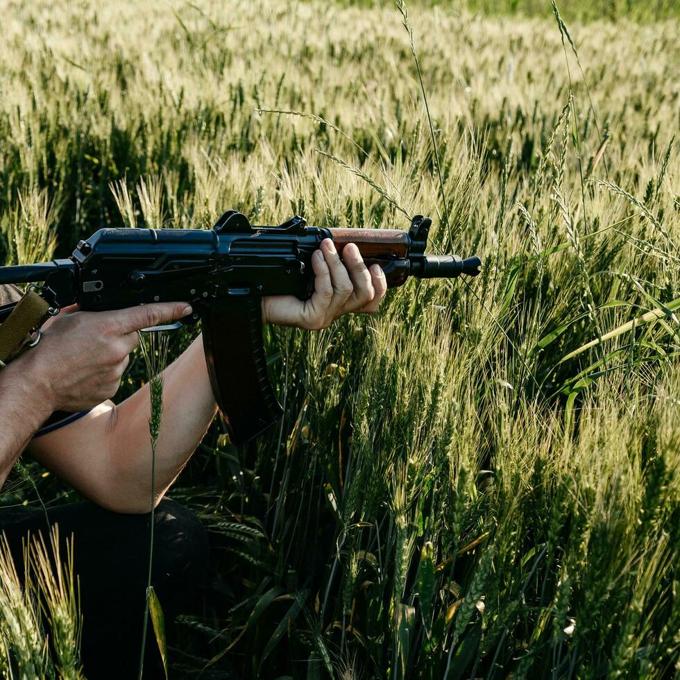 un soldato con un fucile d'assalto militare da combattimento ak 74 si trova in un campo, campi di grano ucraini e guerra. foto