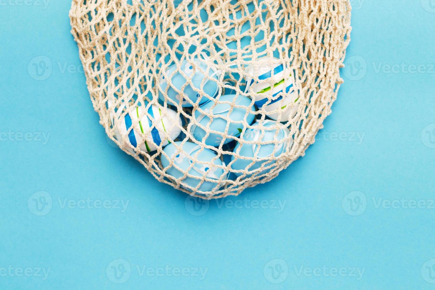 Pasqua colorato dipinto uova nel il cotone corda Borsa su blu sfondo foto