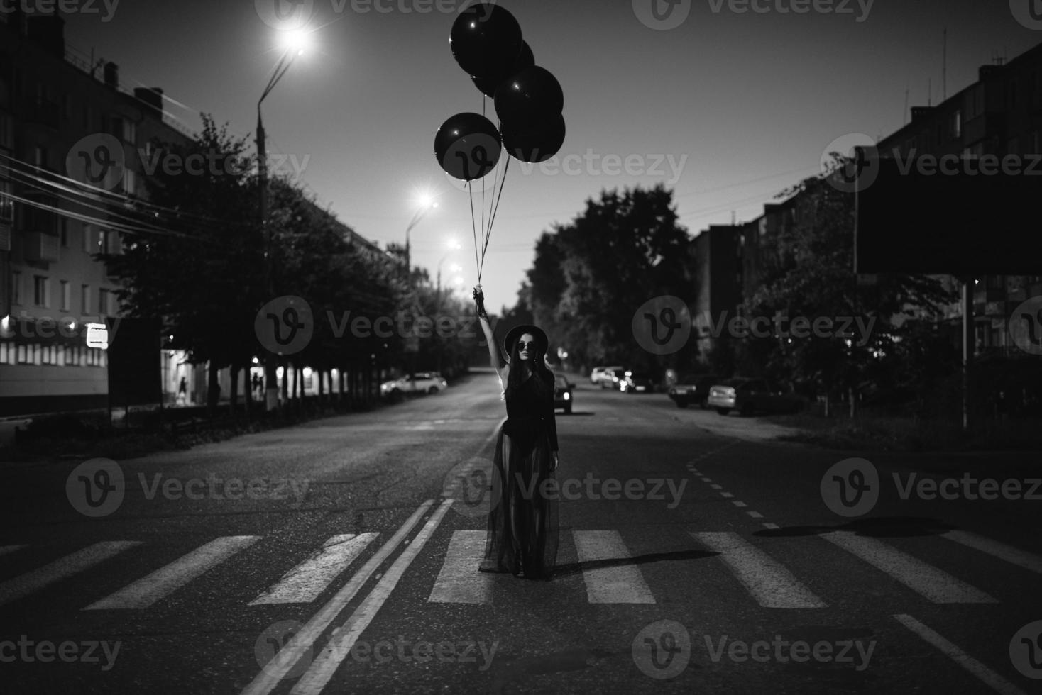 un' ragazza nel nero con nero palloncini nel sua mani pose in piedi su il strada foto