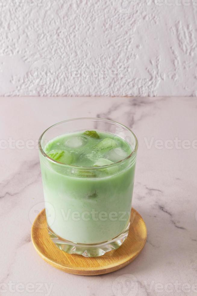 matcha latte macchiato tè con ghiaccio cubi nel un' bicchiere su un' di legno piatto. antiossidante, amino acidi. un' potente Tonico. foto