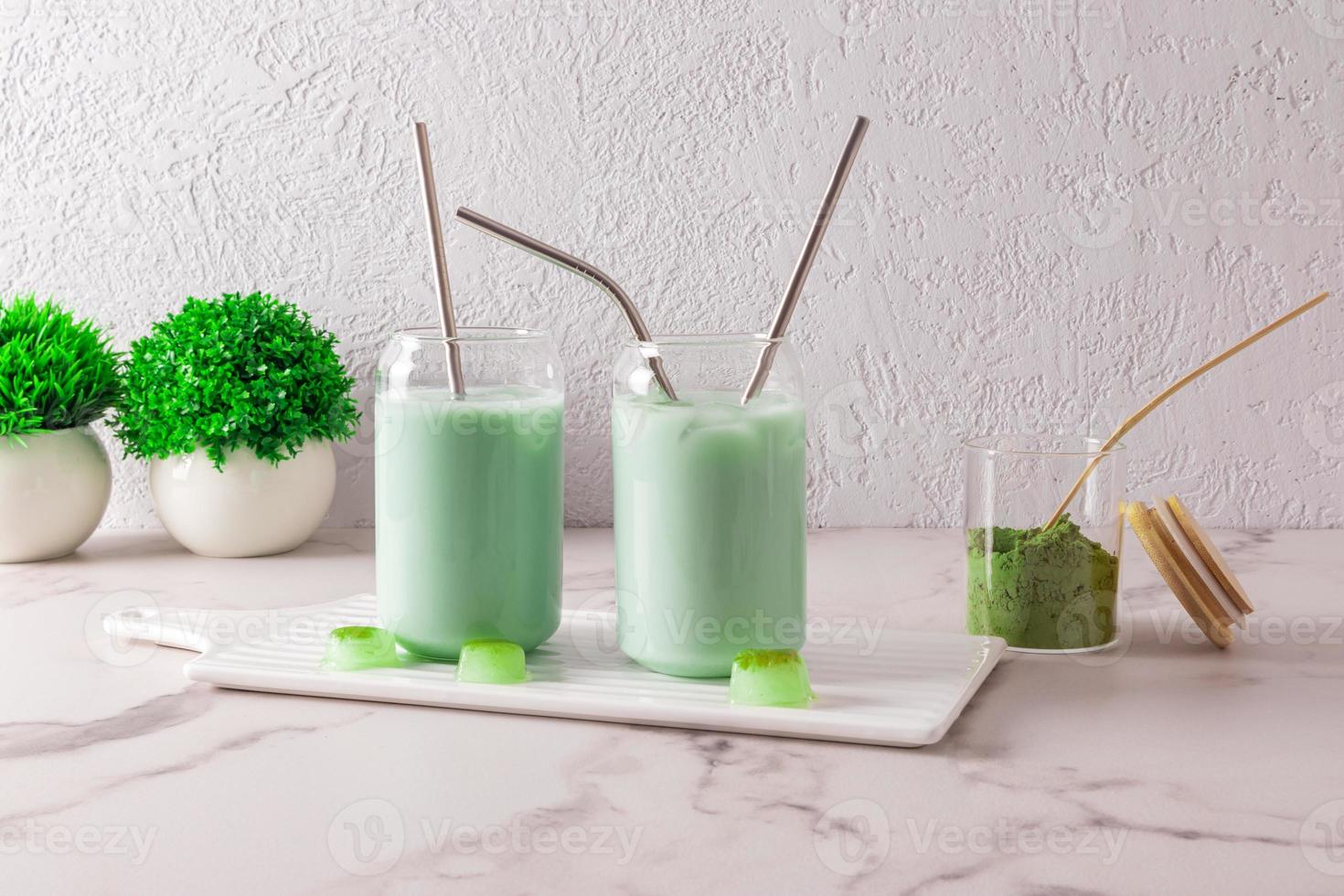 Due moderno bicchieri nel il modulo di un' birra può withiced tè matcha con cannuccia su un' tavola contro un' grigio parete. un alternativa per caffè. caffeina. foto