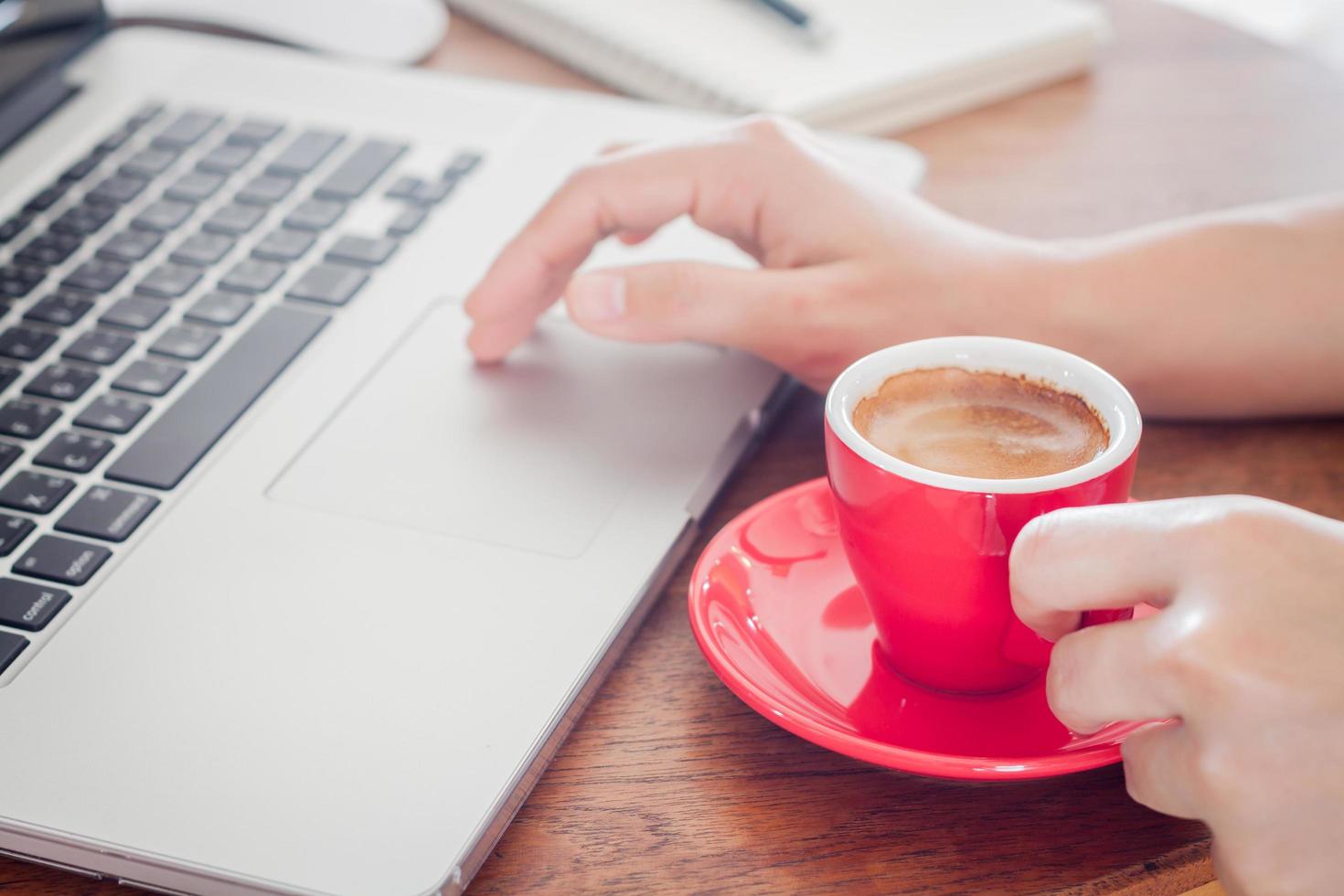 persona in possesso di una tazza di caffè rosso mentre si lavora foto