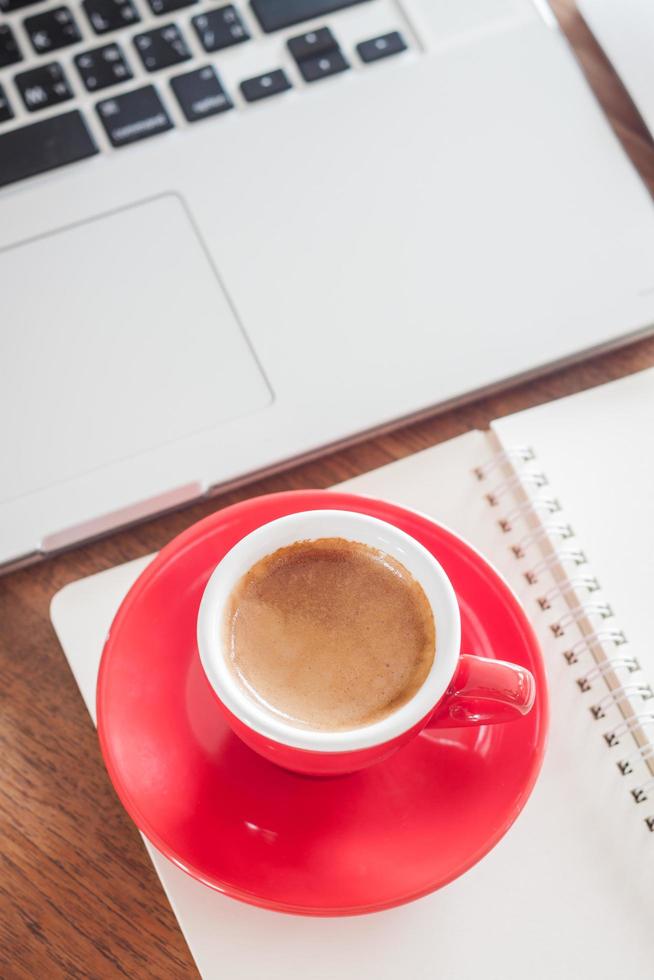 vista dall'alto di una tazza di caffè rosso con un blocco note e un laptop foto