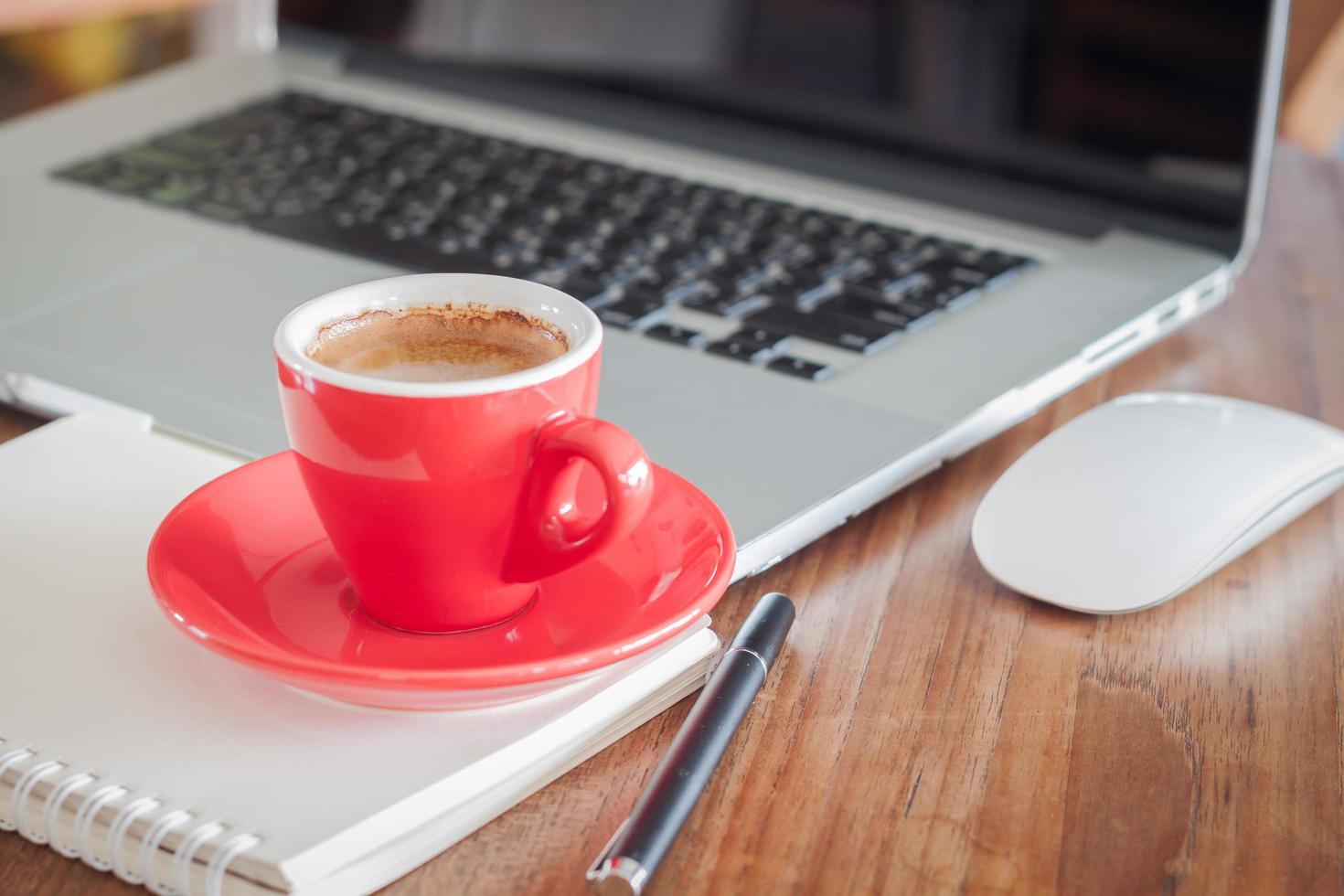 tazza di caffè rosso con un blocco note su un computer portatile foto