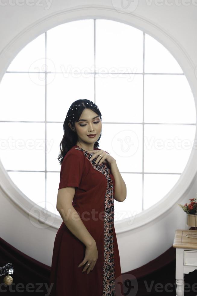 ritratto di un' bella giovane ragazza indossare un' rosso abito, sorridente a il telecamera, in piedi nel decorato Natale vivente camera in casa foto