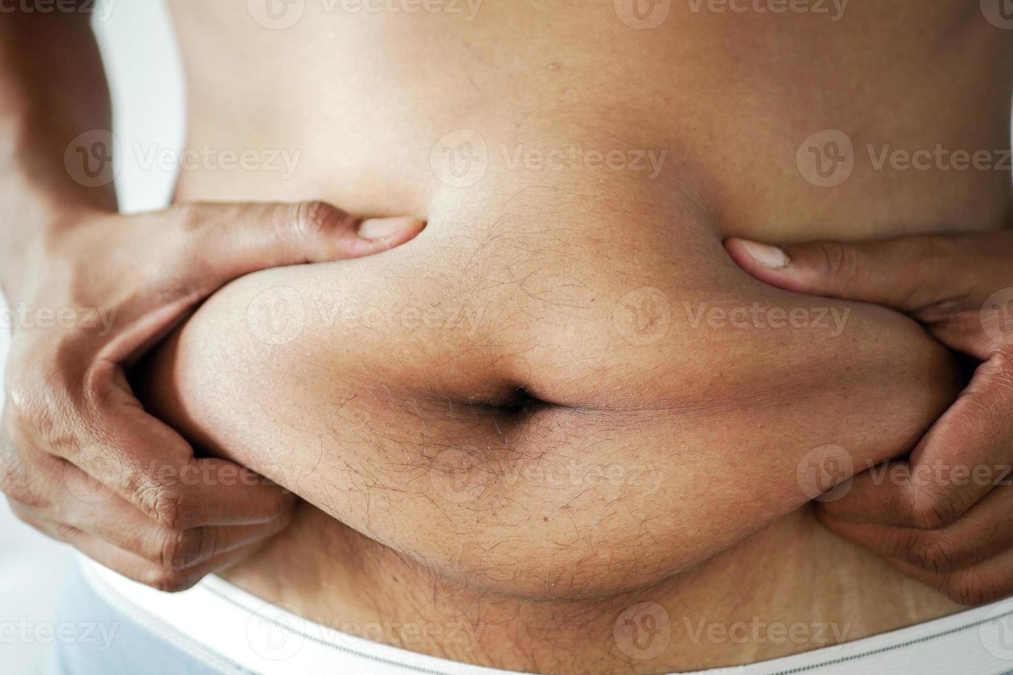 mano d'uomo che tiene il grasso della pancia eccessivo, concetto di sovrappeso foto