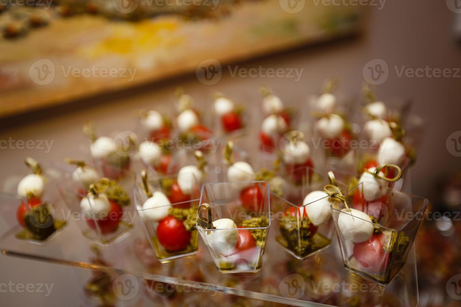 ristorazione per festa. vicino su di Antipasti con ciliegia pomodori, verde olive, oliva olio, formaggio e spezie nel corto bicchieri su legna Marrone tavolo. foto