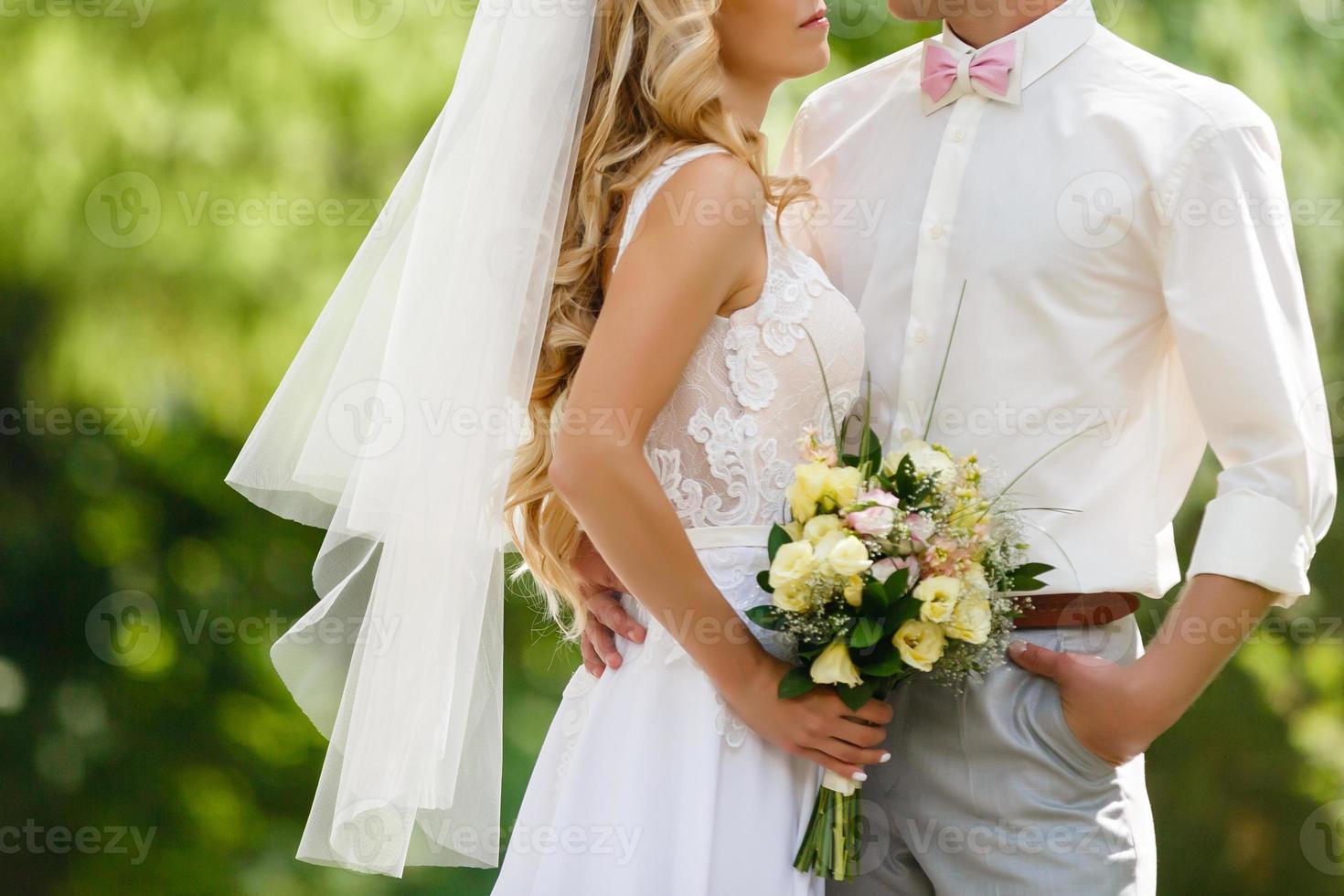 nozze. il sposo nel un' completo da uomo e il sposa nel un' bianca vestito in piedi lato di lato e siamo Tenere mazzi di fiori di bianca fiori e verdura foto