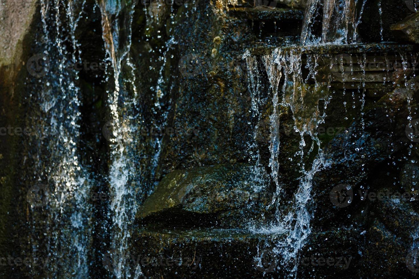 vicino su di acqua spruzzi su rocce a partire dal un' cascata acqua su decorativo pietre foto