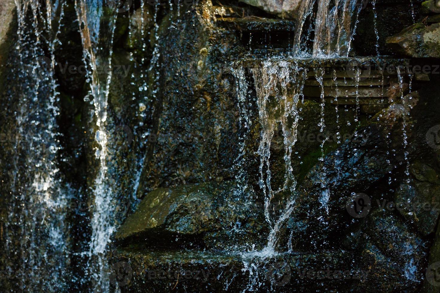 vicino su di acqua spruzzi su rocce a partire dal un' cascata acqua su decorativo pietre foto