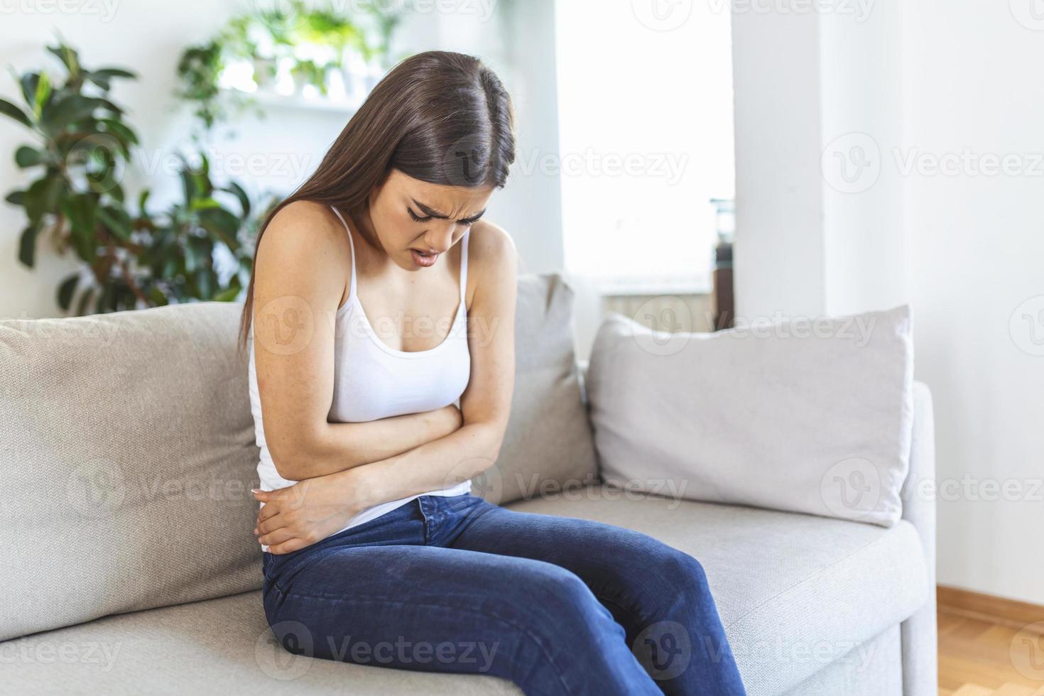 donna nel doloroso espressione Tenere mani contro pancia sofferenza mestruale periodo dolore, dire bugie triste su casa letto, avendo pancia crampo nel femmina Salute concetto foto