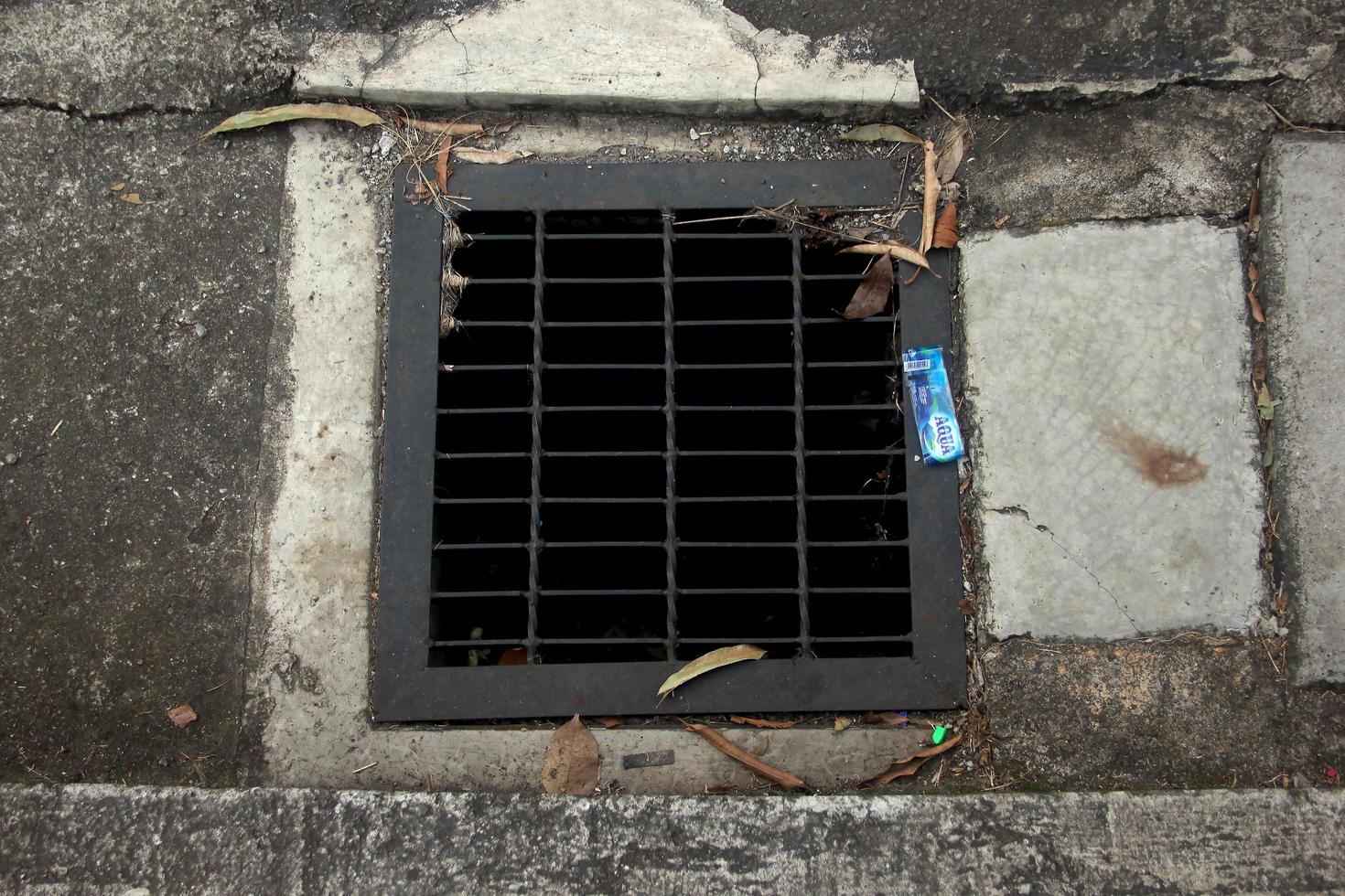 Giacarta, Indonesia - gennaio 21, 2023 - macchiato arrugginito nero marciapiede corso d'acqua con griglia e piazza forma. c'è plastica rifiuto rifiuti in giro esso. foto