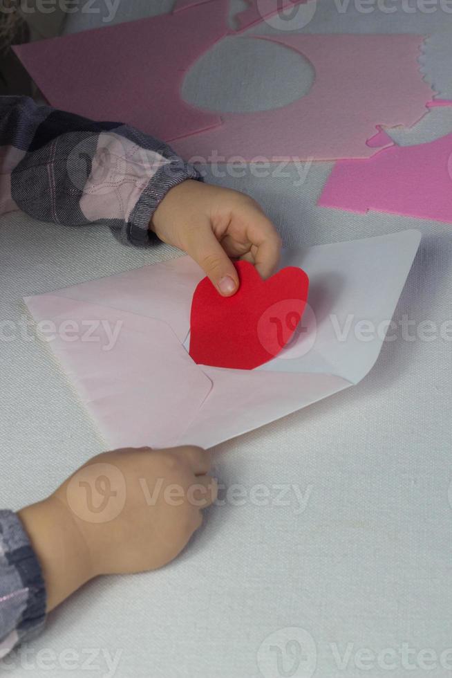 bambino Tenere lettera con rosso carta cuore amore lettera per San Valentino giorno, regalo per madri giorno, piccolo ragazza mettere fatto a mano cuore dentro busta, vacanza saluti a partire dal figlia, finta su per amore auguri foto