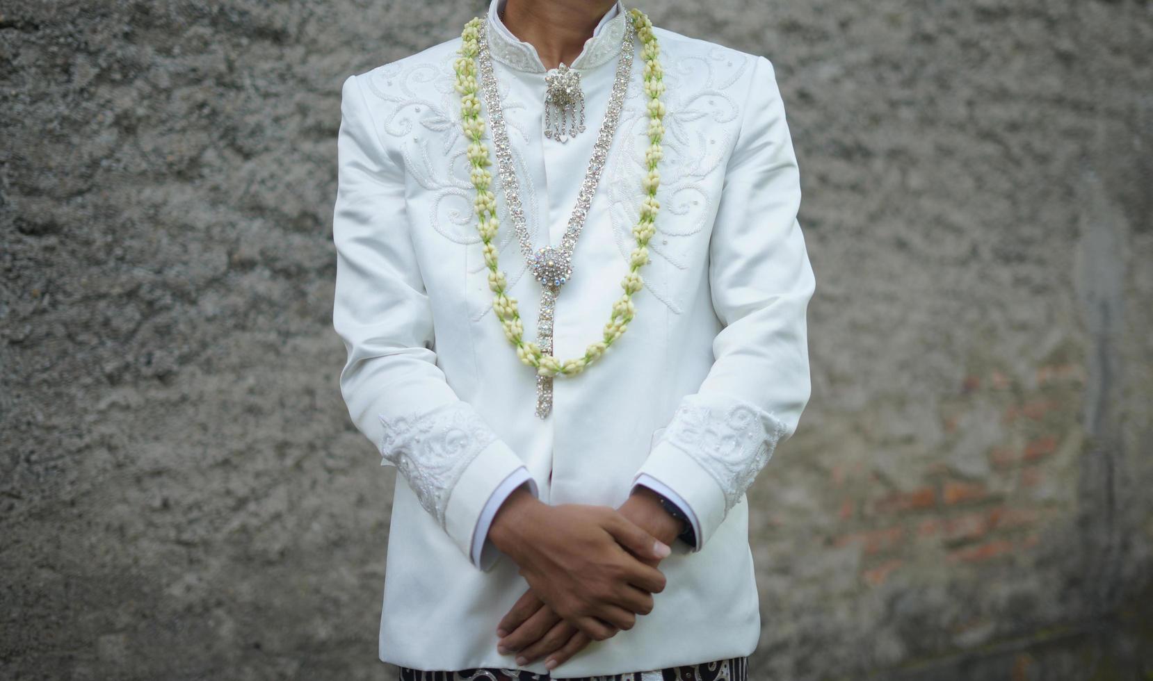 bellissimo sposo Tenere mano mentre indossare nozze vestito con gelsomino e magnolia fiore collana per un' tradizionale nozze cerimonia nel Indonesia foto