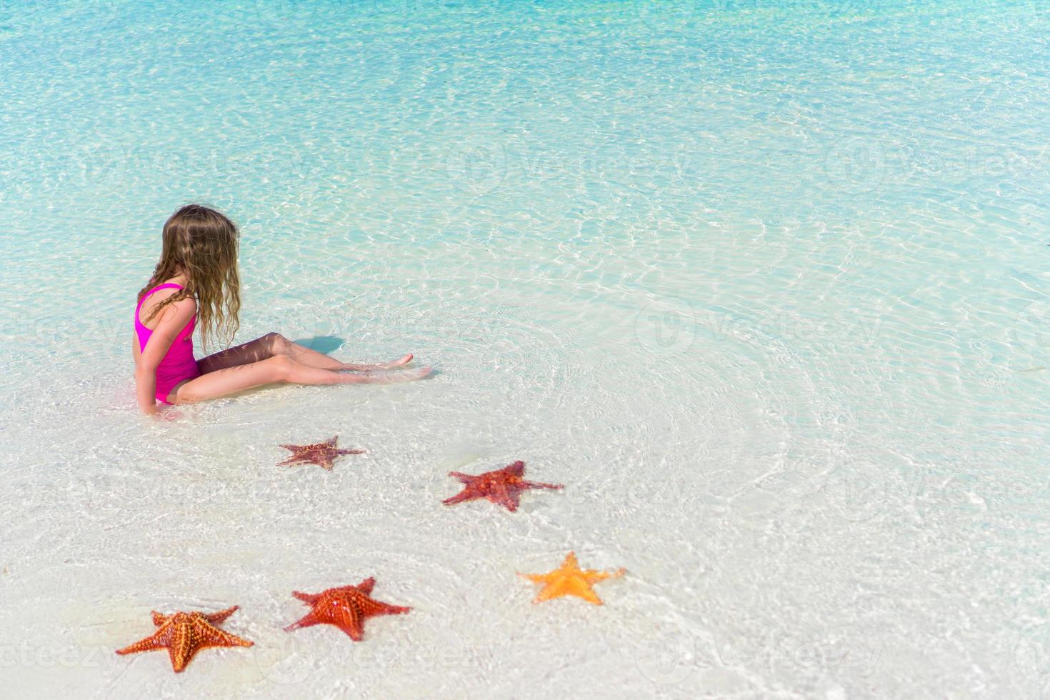 adorabile poco ragazza con stelle marine nel acqua su bianca vuoto spiaggia foto