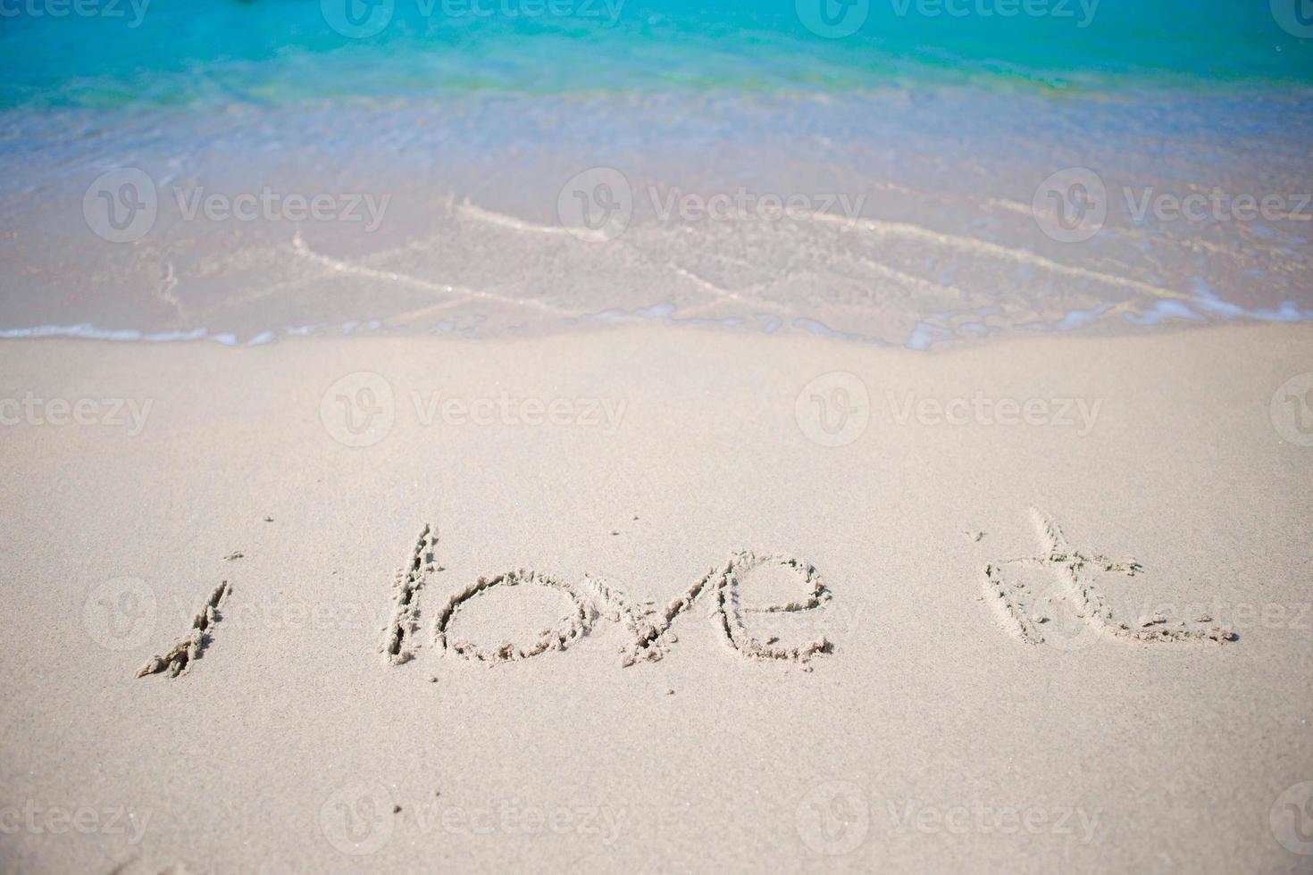parola io amore esso manoscritto su sabbioso spiaggia con morbido oceano onda su sfondo foto