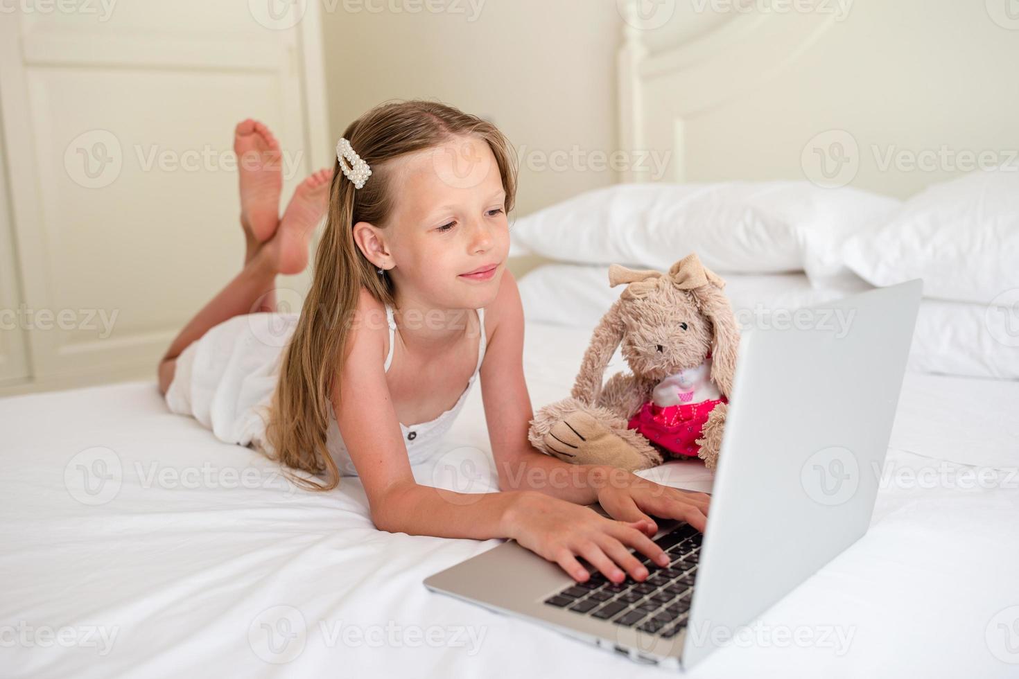 carino poco ragazza fare compiti a casa su il computer portatile foto