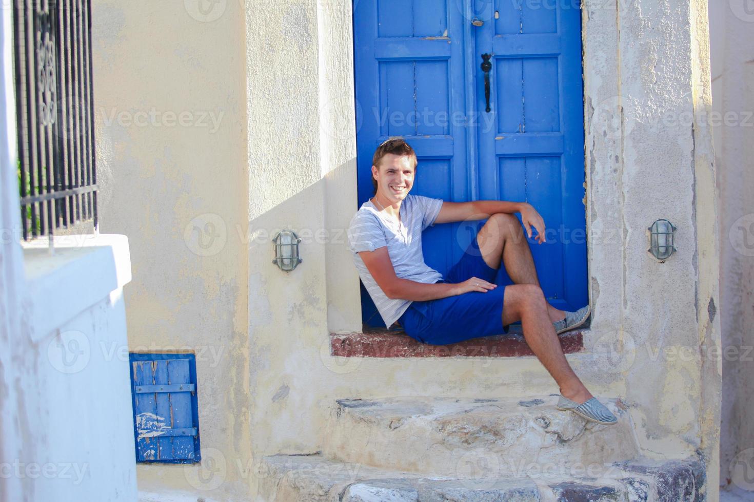 giovane uomo seduta vicino vecchio blu porta di emporio villaggio su il isola Santorini, Grecia foto