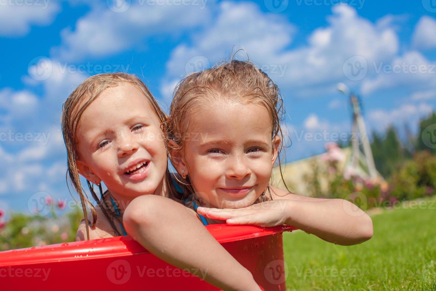 Due carino poco contento ragazze avendo divertimento nel piccolo piscina su il cortile all'aperto e godere vacanza foto