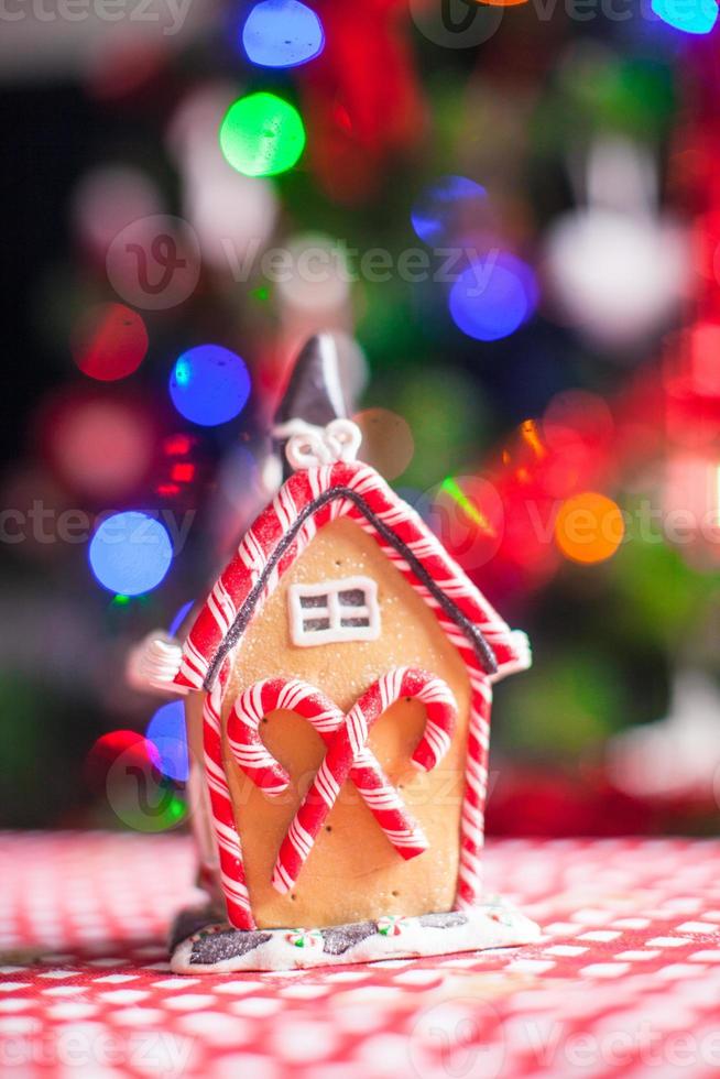 Pan di zenzero Casa decorato di colorato caramelle su un' sfondo di luminosa Natale albero con ghirlanda foto