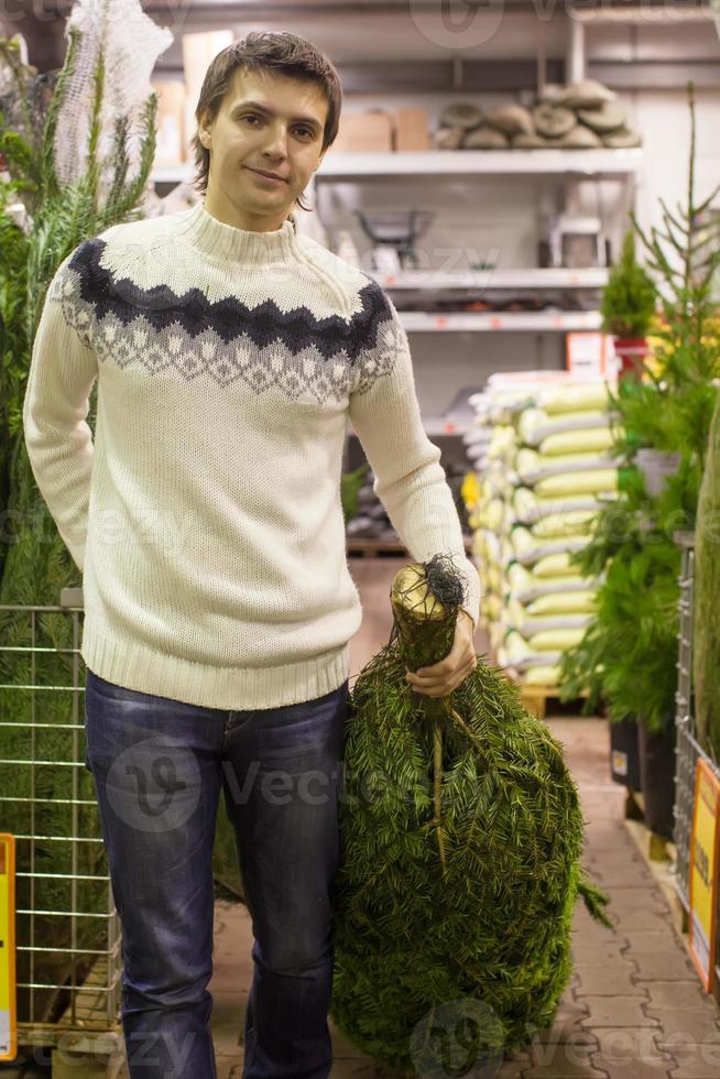 giovane uomo scegliere Natale albero nel il mercato foto