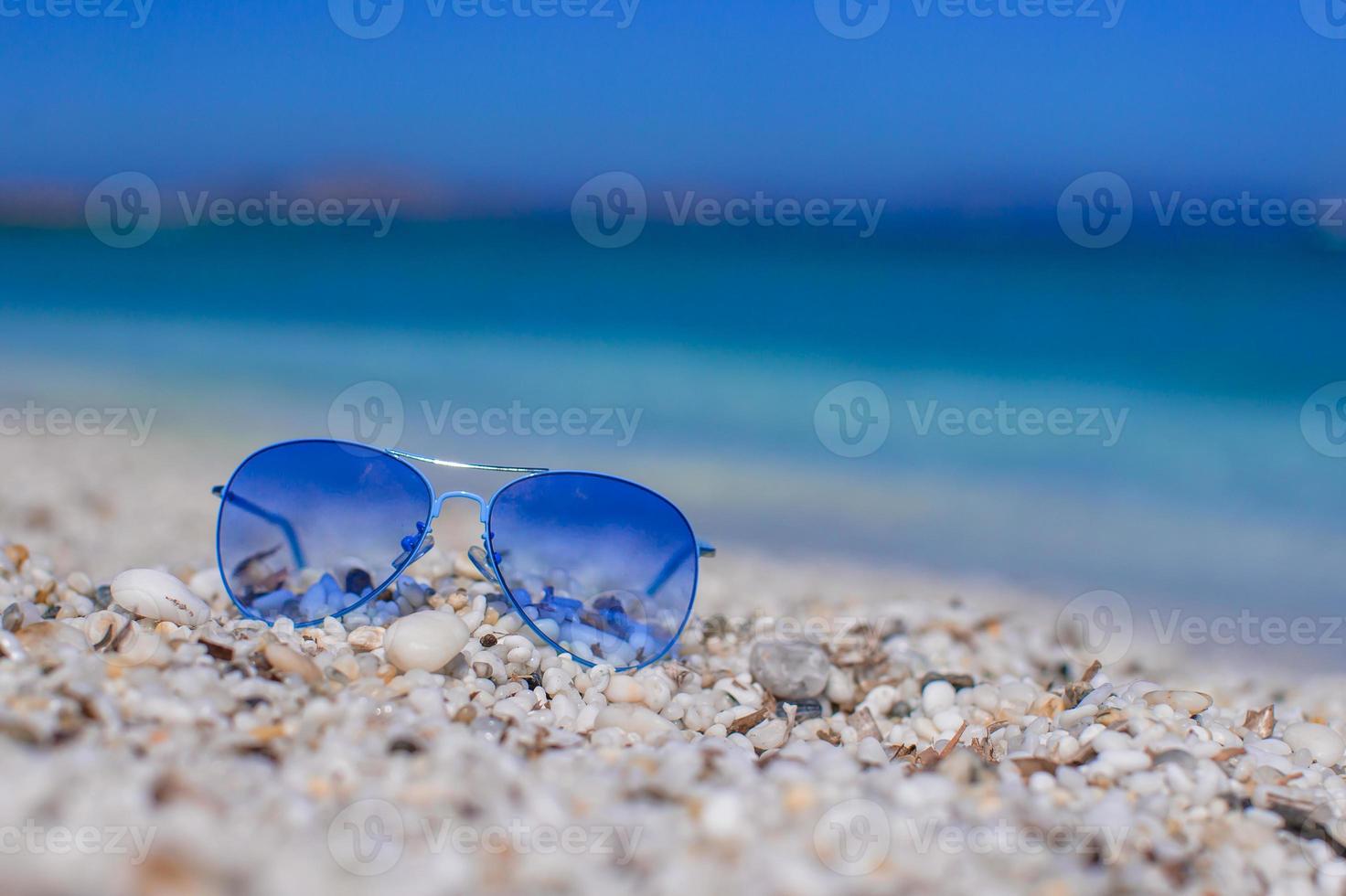 vicino su di colorato blu occhiali da sole su tropicale spiaggia foto