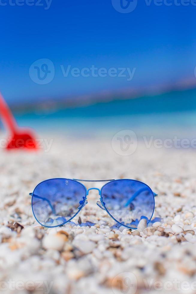 vicino su di colorato blu occhiali da sole su tropicale spiaggia foto