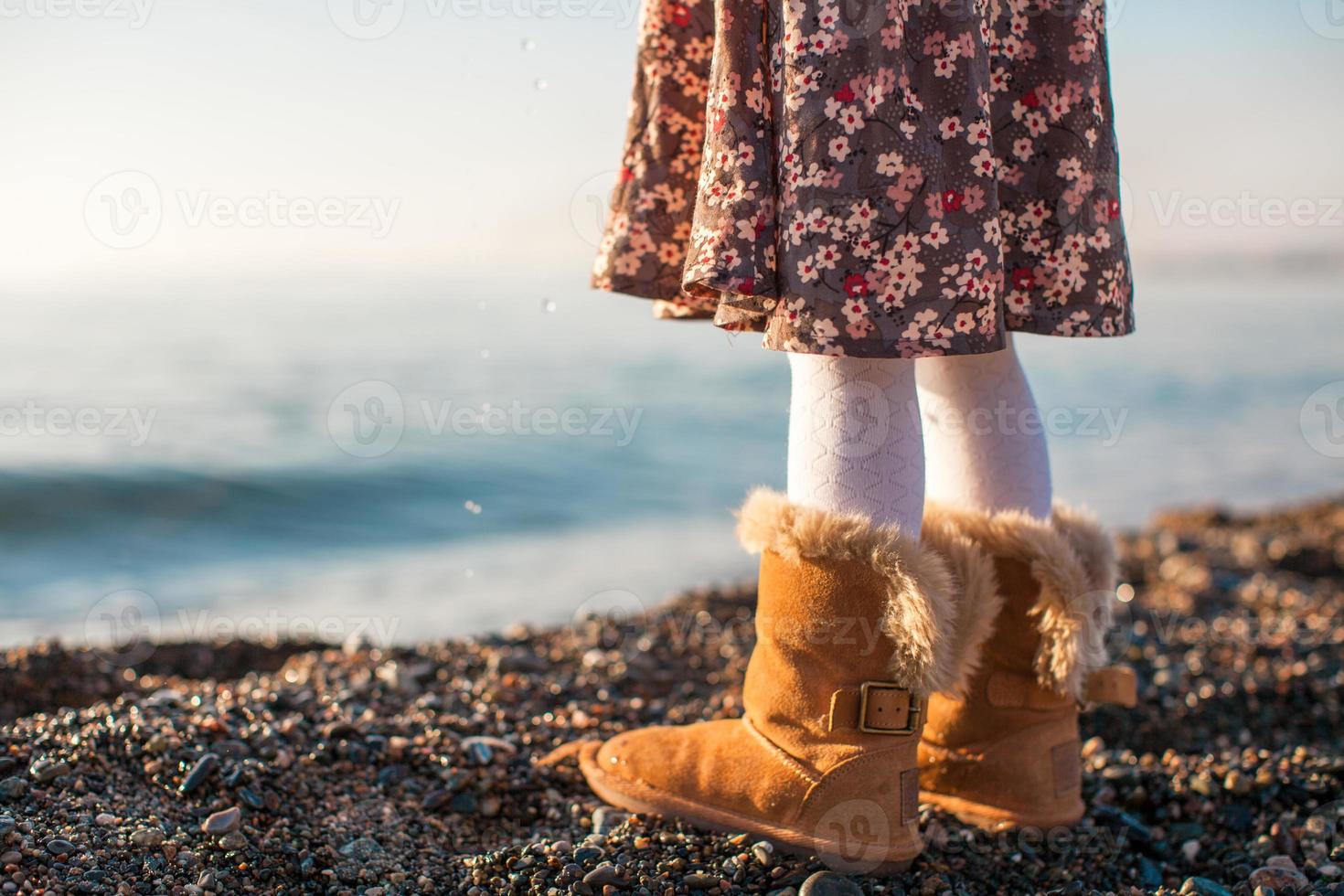 avvicinamento di gambe poco ragazza nel accogliente pelliccia stivali sfondo il mare foto