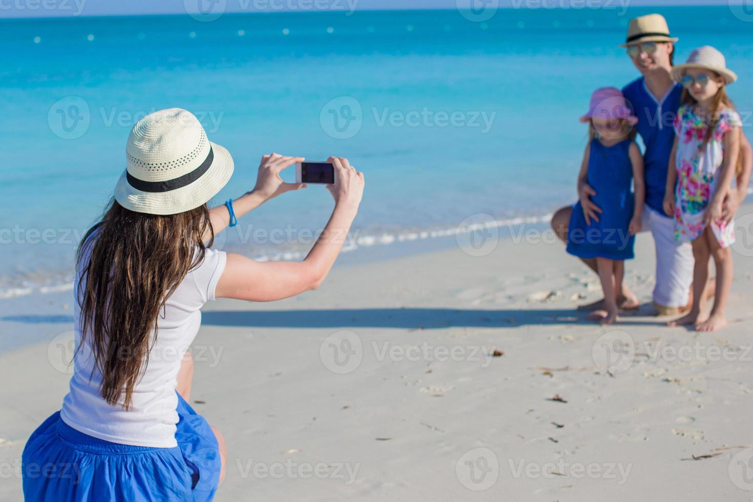 giovane madre fabbricazione foto su Telefono di sua famiglia a il spiaggia