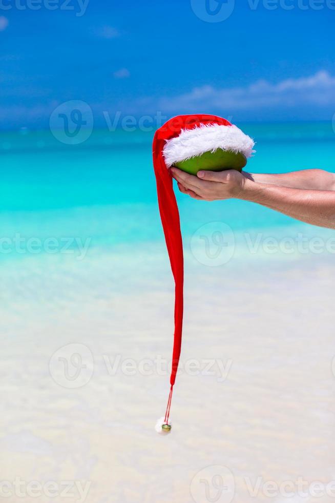 Noce di cocco con Santa cappello nel maschio mani contro il turchese mare foto