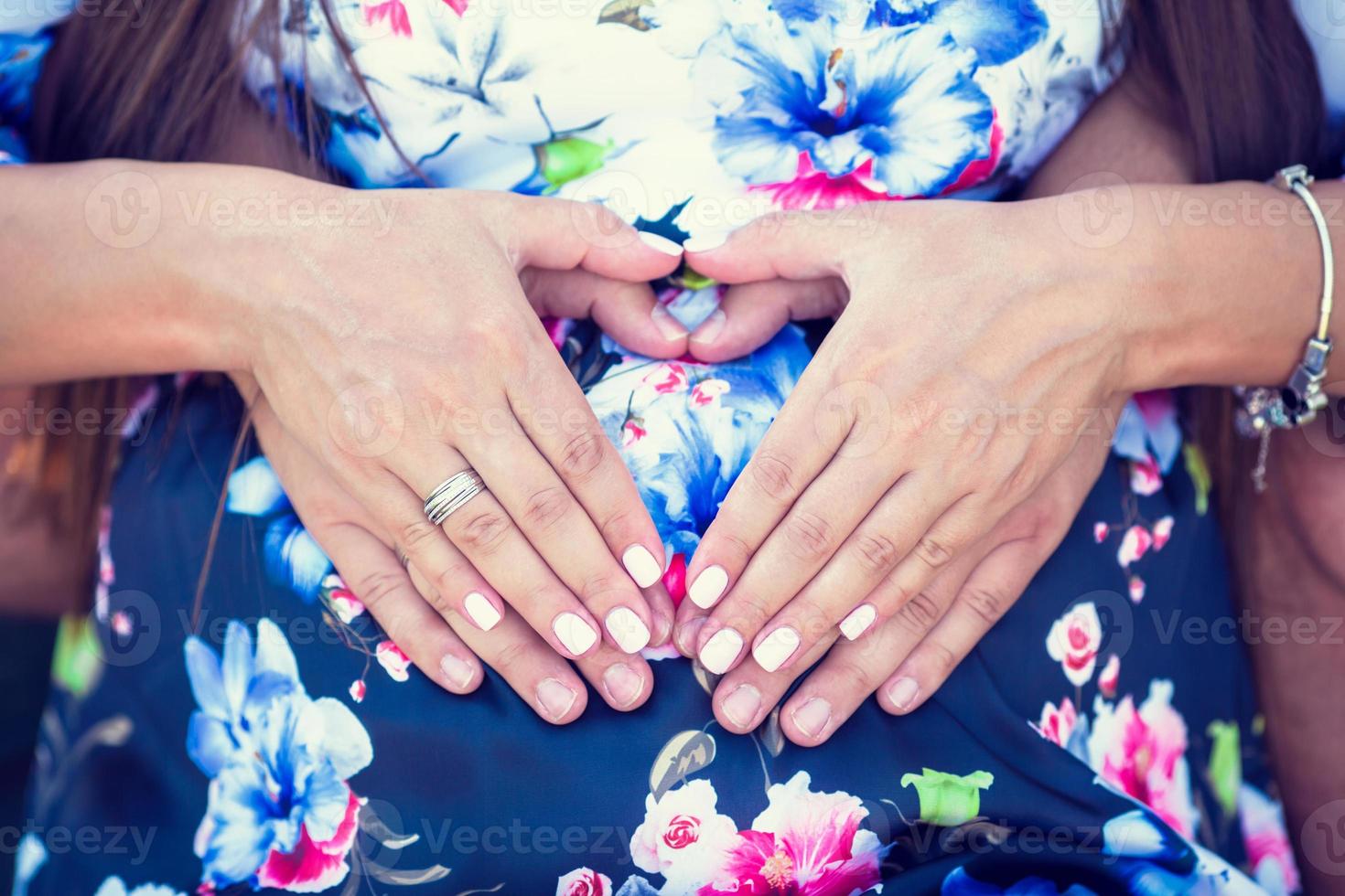 genitori mani fabbricazione un' cuore su il pancia di il incinta madre foto