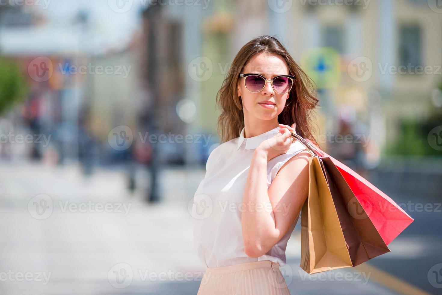 giovane contento ragazza con shopping borse all'aperto. ritratto di un' bellissimo contento donna in piedi su il strada Tenere shopping borse sorridente foto