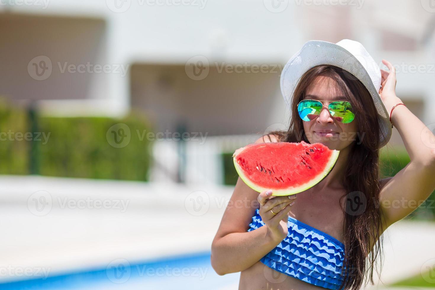 giovane donna nel cappello e occhiali da sole con anguria rilassante vicino piscina foto